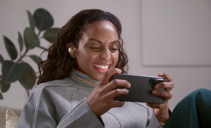 Woman sitting in a living room wearing LinkBuds S, watching video on her smartphone